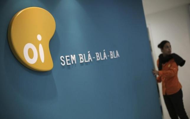 A woman stands next to the logo of Brazil's largest fixed-line telecoms group Oi, inside a shop in Sao Paulo October 2, 2013. REUTERS/Nacho Doce